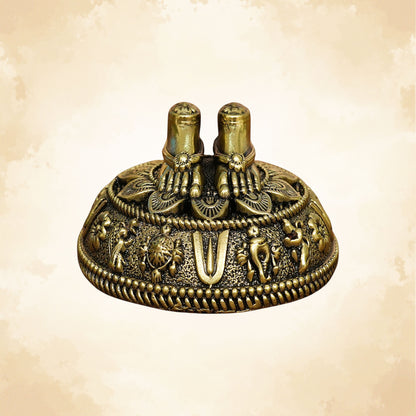 Handcrafted brass Charan Paduka placed on an ornate circular base with elephant and floral carvings.